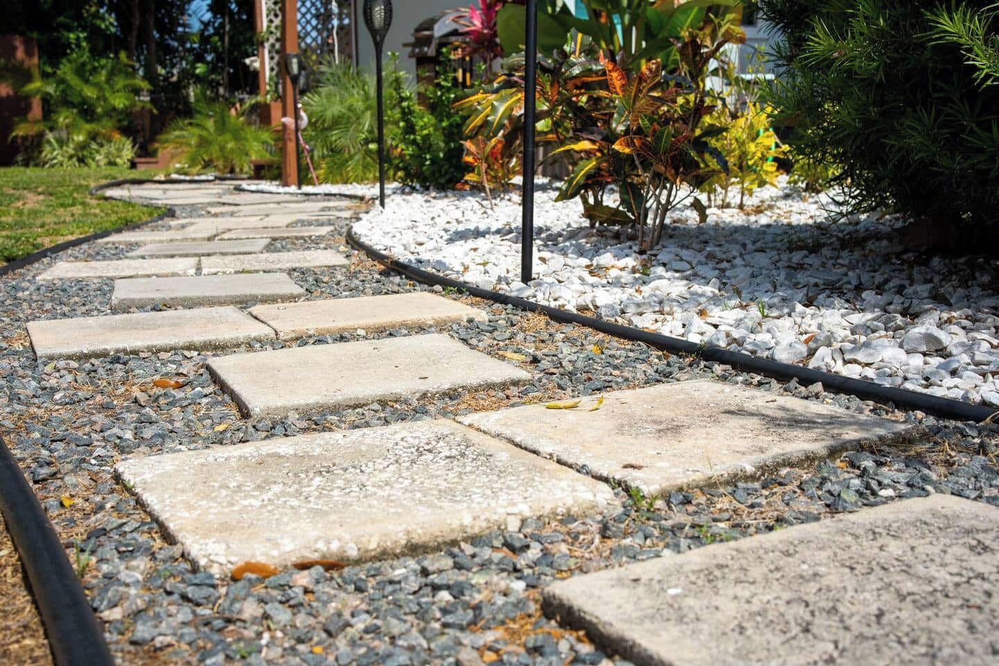 Un vialetto in giardino con pietre di passaggio, circondato da ghiaia e piccole piante.