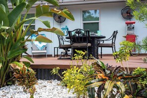 Une terrasse extérieure avec une table et des chaises, entourée de différentes plantes et agrémentée d’une sculpture de verre décorative.