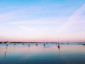 A calm body of water with multiple boats anchored, clear skies, and a distant shoreline.