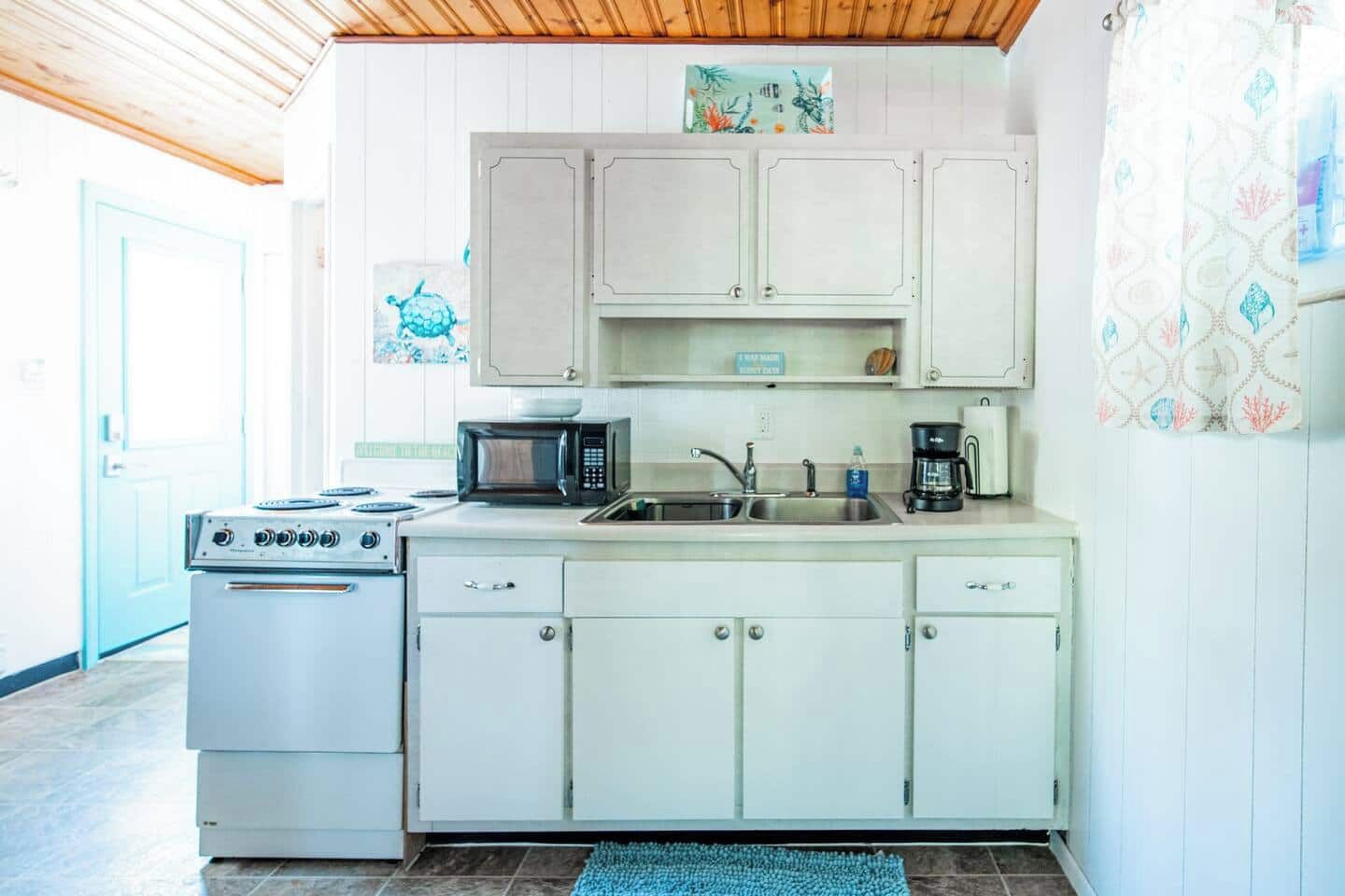 Cocina compacta con muebles blancos, estufa, microondas y pileta.