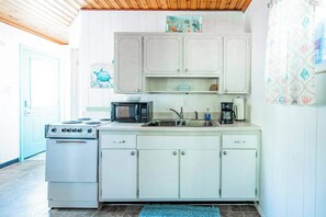 Una cucina compatta con mobili bianchi, un fornello, un forno a microonde e un lavello.