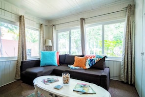A cozy living room with a dark-colored sofa, a white coffee table, and a window with curtains.