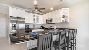 Una cocina moderna con armarios blancos, electrodomésticos de acero inoxidable, una isla central con cuencos azules y un ventilador de techo.