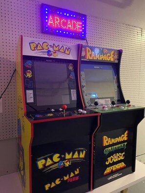 Two arcade machines, one labeled 'PAC-MAN' and the other 'RAM-PAGE,' with a sign above indicating 'ARCADE.' - Anna Maria Island Getaway | Pool + Game Room | IMG (Bradenton)