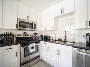 Una cocina moderna con gabinetes blancos, electrodomésticos de acero inoxidable y encimera negra.