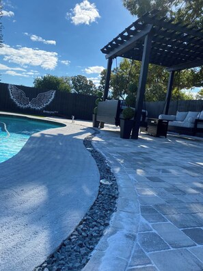 Una piscina con un deck de piedra y una pérgola.