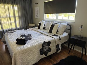 A bedroom with a bed, a nightstand, a lamp, a window with curtains, and a wall art piece. - Anna Maria Island Getaway | Pool + Game Room | IMG (Bradenton)
