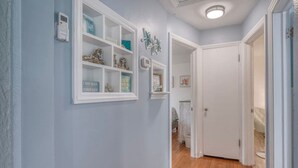 Un pasillo con paredes azul claro, estantes blancos con adornos y una puerta blanca que da a otra habitación.