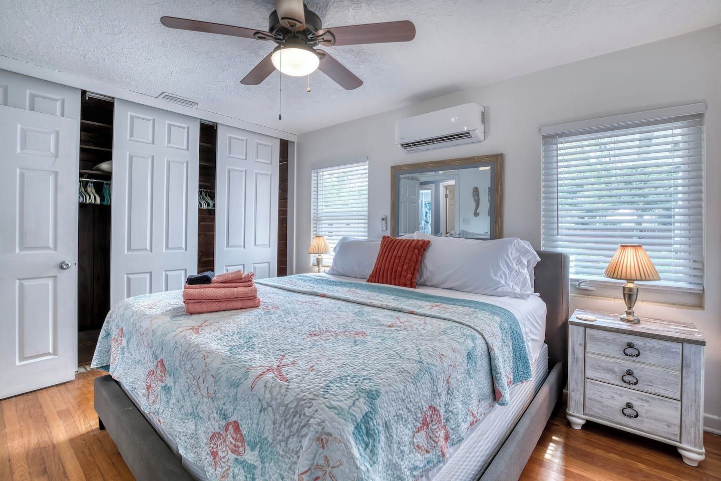 Une chambre à coucher comprenant un lit, un ventilateur de plafond, un appareil de climatisation, une table de chevet avec une lampe et une armoire avec un miroir.