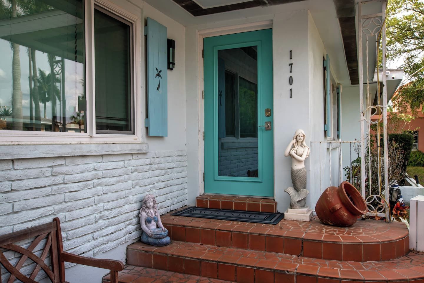 Uma casa com porta turquesa, fachada de tijolos brancos e uma pequena estátua de sereia nos degraus.