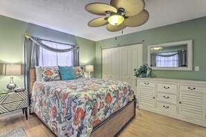 A bedroom with a bed, bedside lamps, a ceiling fan, a dresser, and a mirror.