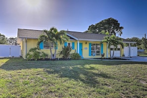 A single-story building with a flat roof, a front porch, and a small garden area with palm trees.