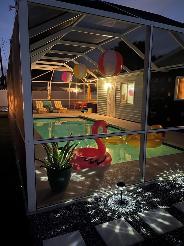 A glass-enclosed pool area with lounge chairs and a flamingo float.