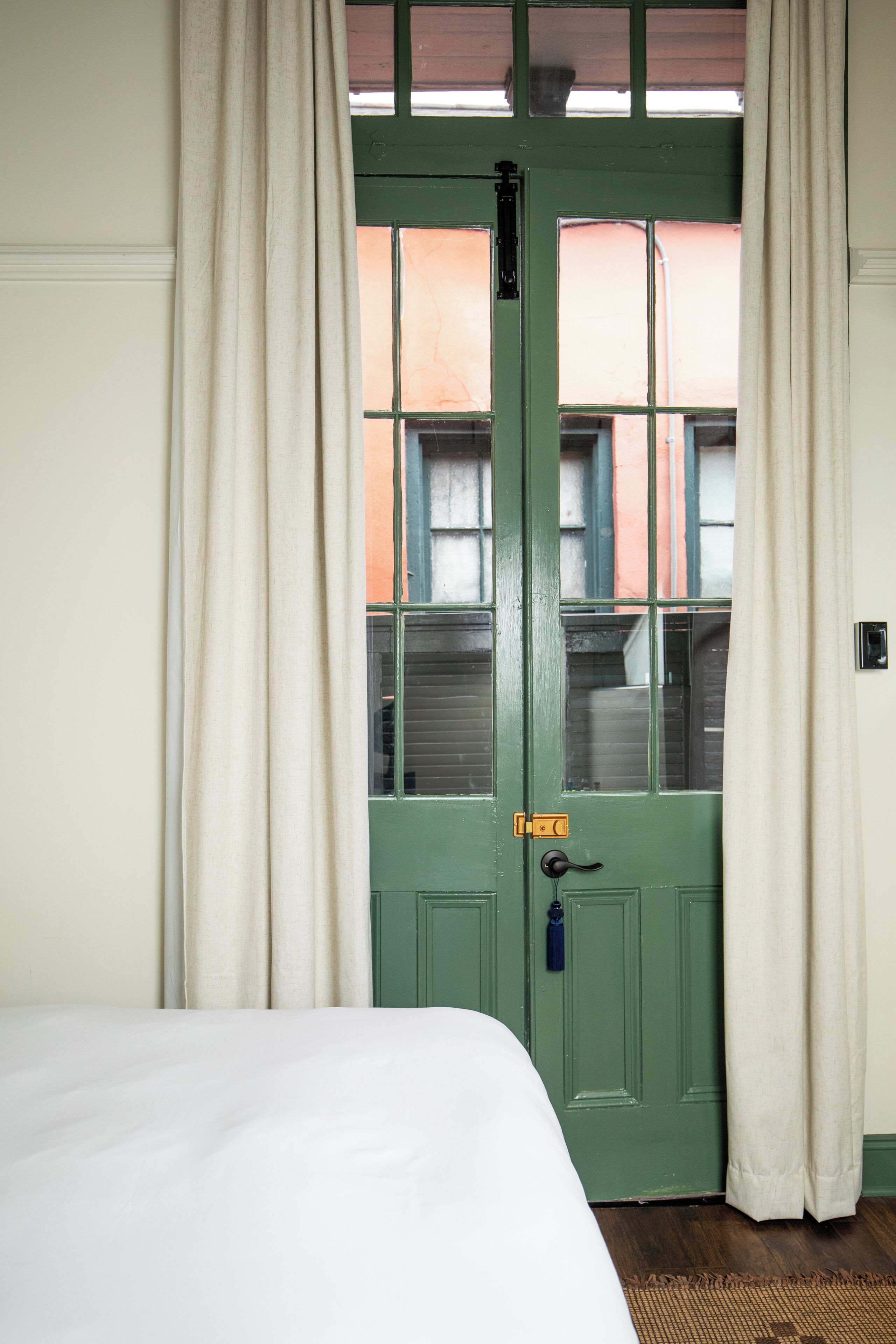 Een kamer met een groene deur, witte gordijnen en een bed.