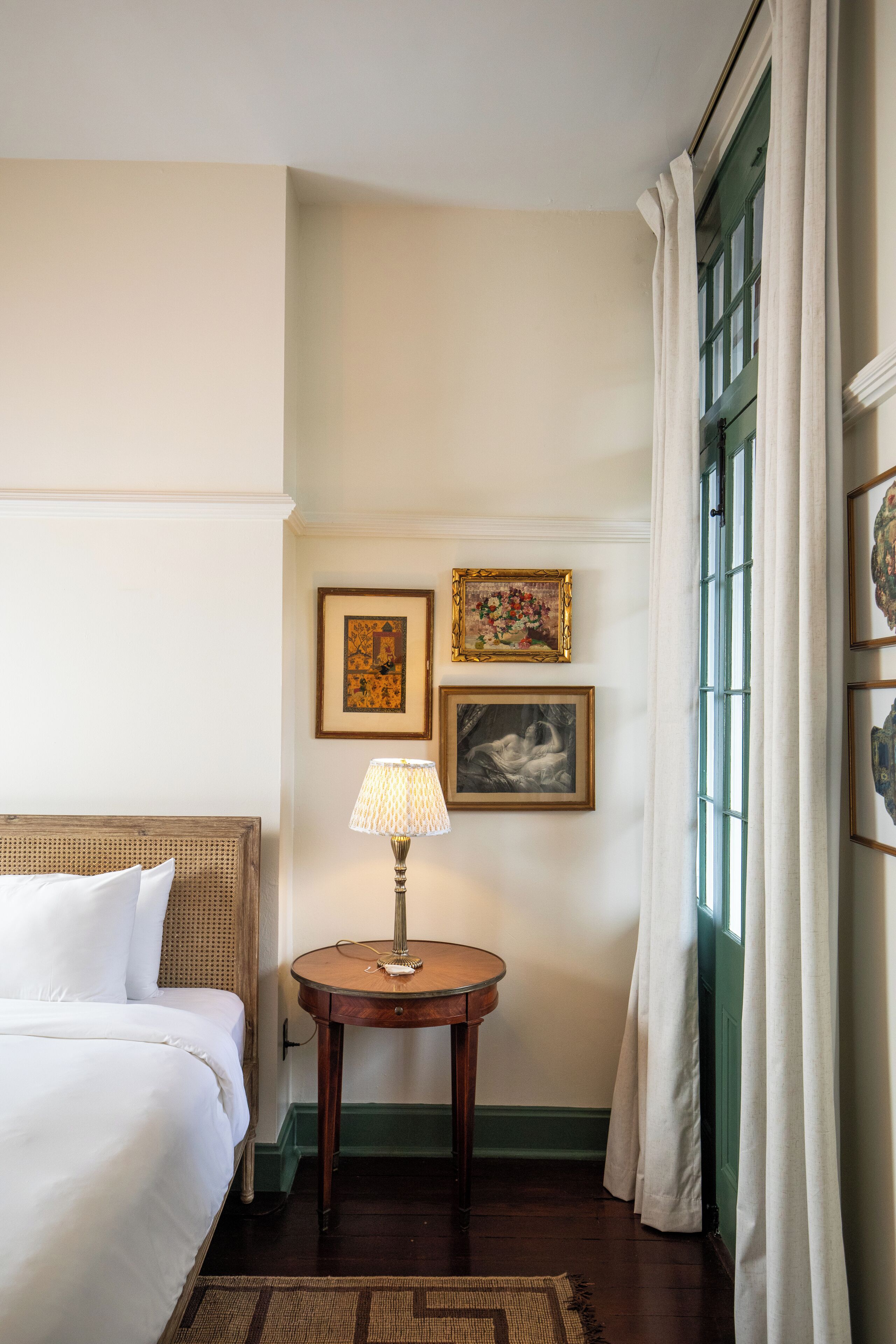 A hotel room with a bed, a round table with a lamp, and two framed pictures on the wall.