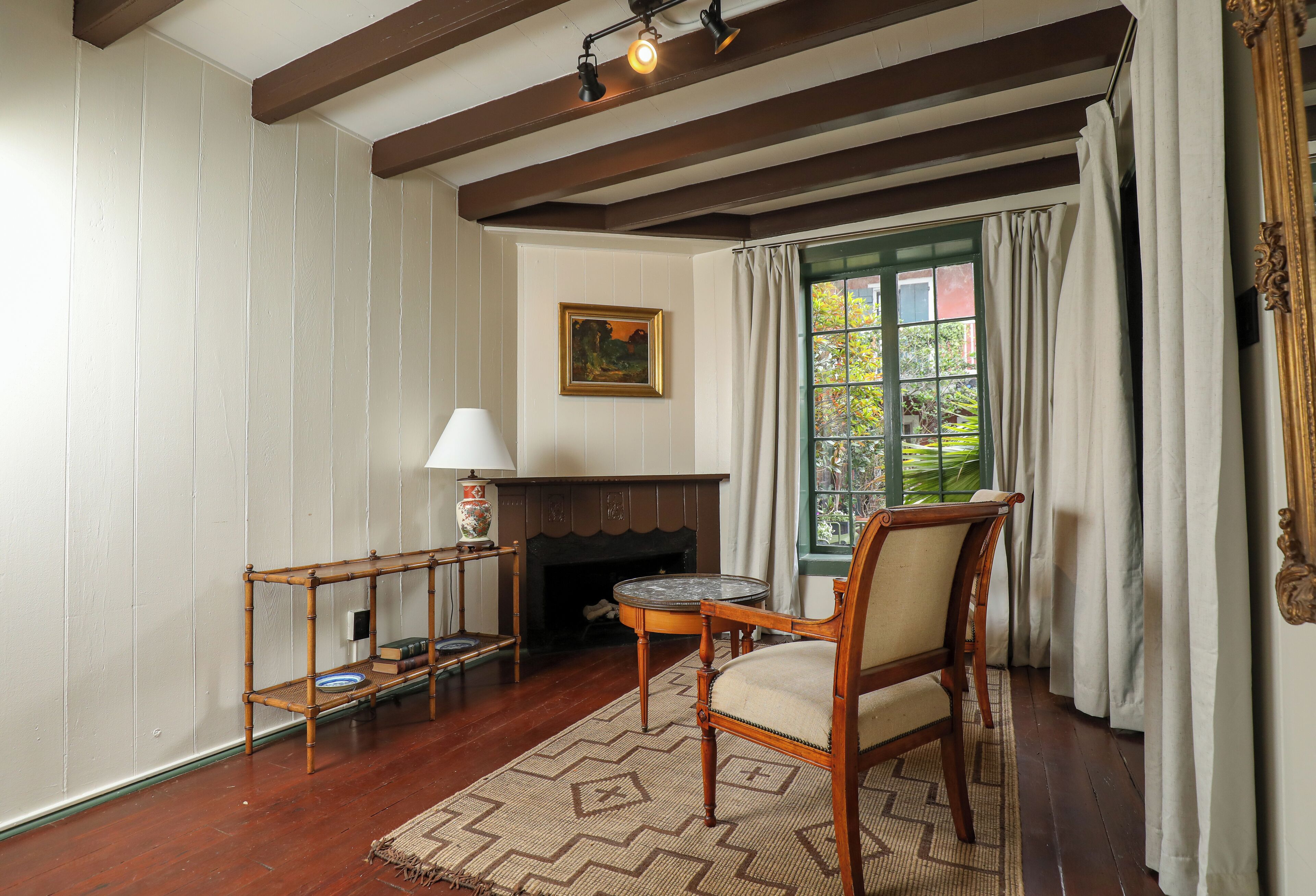 A room with a wooden floor, a fireplace, a table with chairs, a lamp, and a window with curtains.