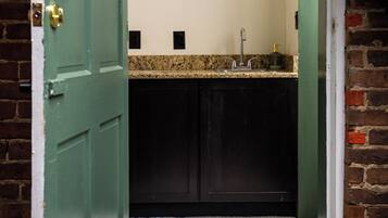 A bathroom with a green door, a white tiled floor, and a granite countertop with a sink.