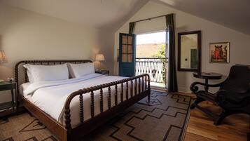 Ein Schlafzimmer mit einem hölzernen Bett, Deckenventilator, einem Fenster mit Vorhängen, einem kleinen Tisch und einem Sessel.