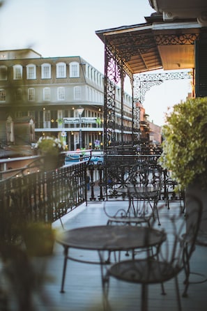 A balcony with metal railings and tables, overlooking a street with buildings and a bridge. - The Celestine (New Orleans)