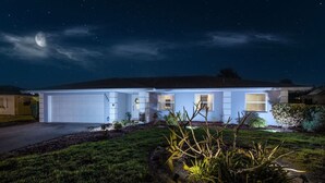 Una casa moderna con garaje, césped cuidado y un cielo nocturno despejado con estrellas visibles.