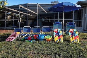 A row of beach chairs and umbrellas in front of a building with a covered patio area. - Waterfront Heated Pool | AMI • Siesta • IMG (Sarasota)