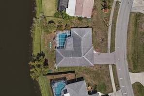 A residential property with a large swimming pool, a covered patio, and a view of a lake. - Waterfront Heated Pool | AMI • Siesta • IMG (Sarasota)