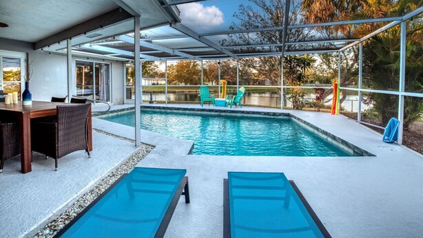 Una piscina con un porche cubierto, sillas de descanso y una mesa de comedor.