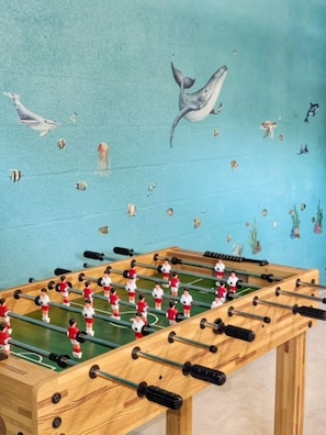 A foosball table with a blue wall in the background. - Waterfront Heated Pool | AMI • Siesta • IMG (Sarasota)