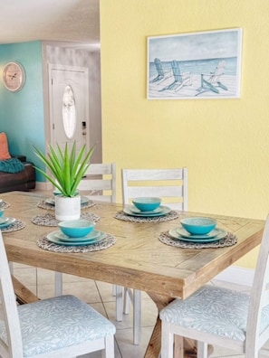 A dining area with a wooden table, white chairs, and blue tableware. - Waterfront Heated Pool | AMI • Siesta • IMG (Sarasota)
