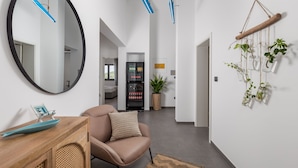 Ein modernes Interieur mit einem runden Spiegel, einem Holzkonsolentisch, einem Ledersessel und einer hängenden Pflanzenanordnung.