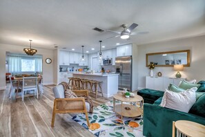 A modern kitchen with white cabinets, a stainless steel refrigerator, and a dining area with wicker chairs and a table. - AMI Getaway | Heated Pool • Game Room • Putting (Bradenton)