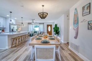 A modern kitchen with a central island, dining area with a wooden table, and a ceiling fan. - AMI Getaway | Heated Pool • Game Room • Putting (Bradenton)