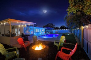 An outdoor patio area with a pool, fire pit, and seating. - AMI Getaway | Heated Pool • Game Room • Putting (Bradenton)
