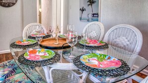 Comedor con mesa de vidrio rodeada de sillas de mimbre, cada una con un posavasos estampado con motivos florales.