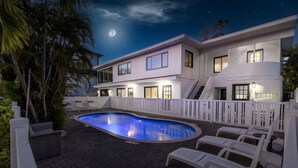 Una casa moderna con piscina, ringhiere bianche e una luna nel cielo.