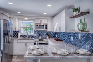 A modern kitchen with white cabinets, a central island with seating, a microwave, and a stove.
