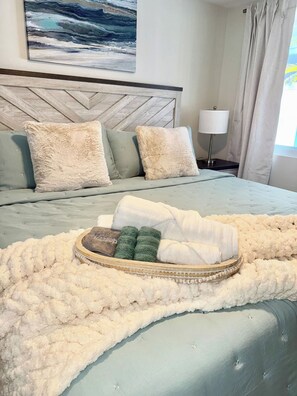A neatly made bed with a fluffy white blanket, a headboard with a geometric pattern, and a bedside table with a lamp. - Steps to Anna Maria Island Beaches + Private Heated Pool (Holmes Beach)