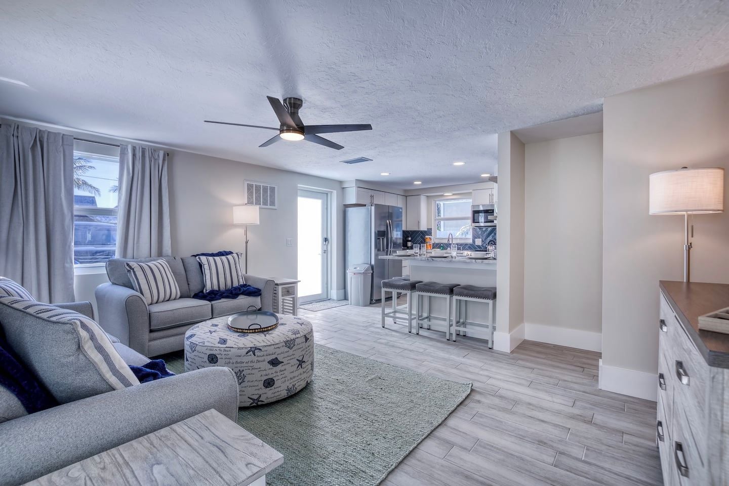 A modern living room with a sofa, ottoman, and a ceiling fan.