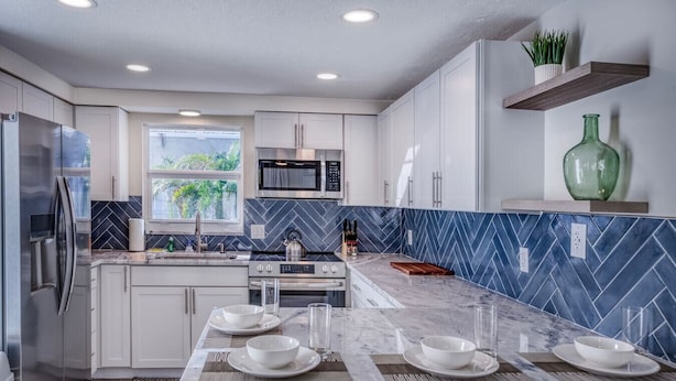 A modern kitchen with white cabinets, a central island with seating, a microwave, and a stove. - Recover by the Seas at Solace East - prvt pool (Holmes Beach)