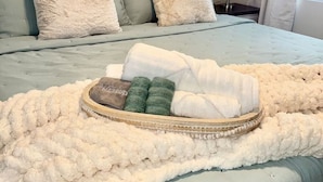 A neatly made bed with a fluffy white blanket, a tray with towels and toiletries, and a headboard with a geometric pattern. - Recover by the Seas at Solace East - prvt pool (Holmes Beach)