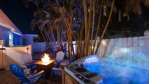 Un jacuzzi con panel de control, rodeado de sillas y una chimenea, con palmeras y una valla blanca al fondo.