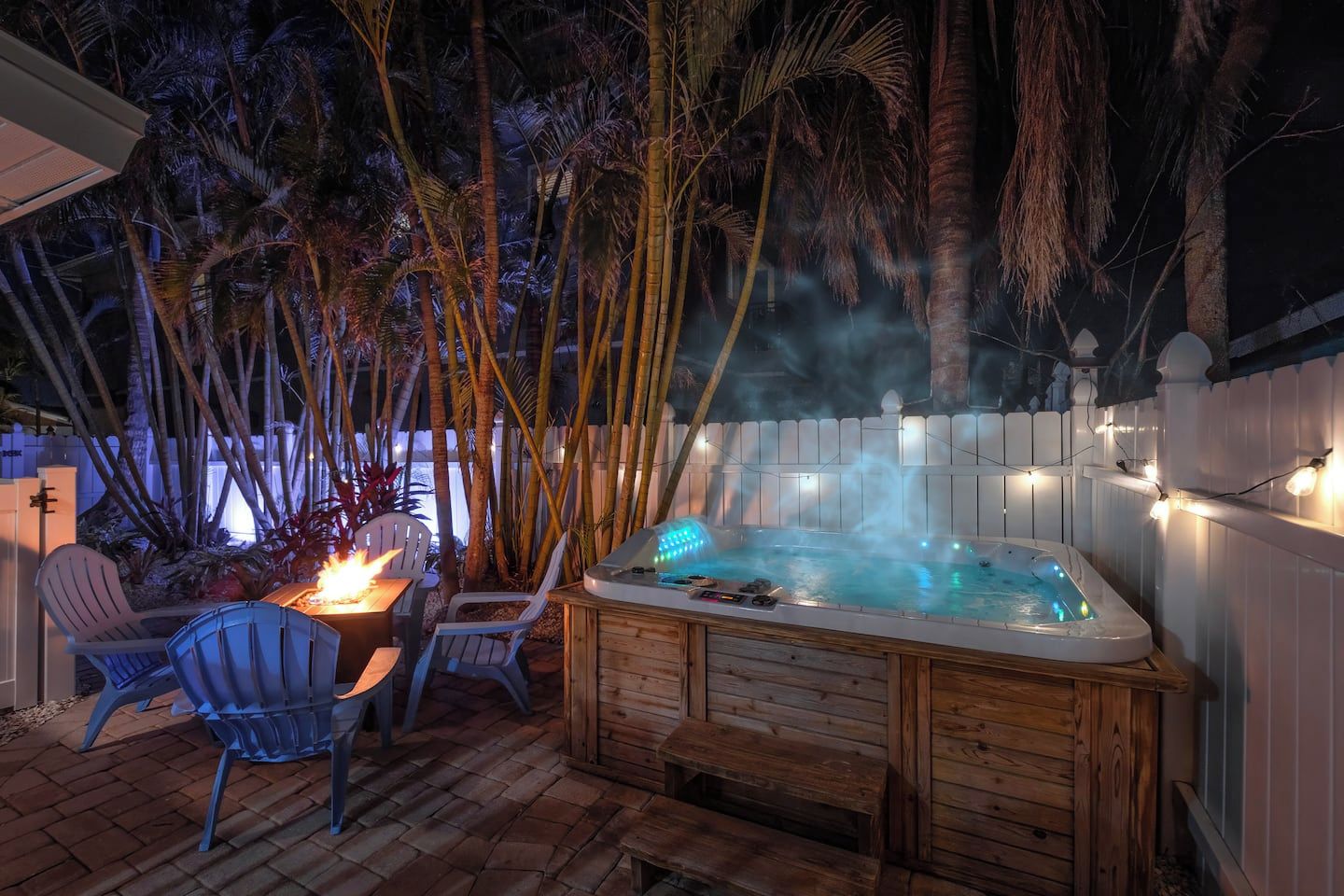 Ein Whirlpool mit Holzterrasse, umgeben von Palmen und einem weißen Zaun.