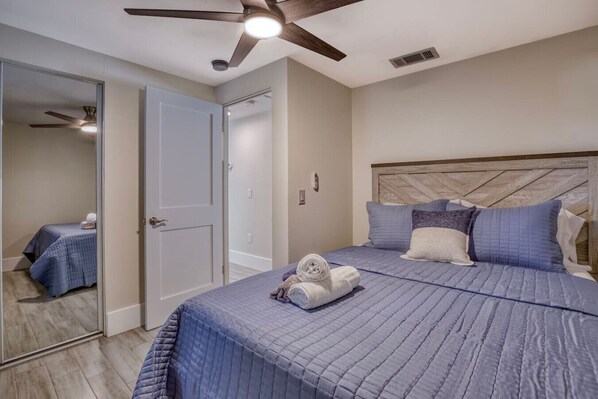 A bedroom with a bed, a ceiling fan, a door, and a mirror. - Retreat at Solace West-Hot Tub/Fire Pit/Sunsets (Holmes Beach)