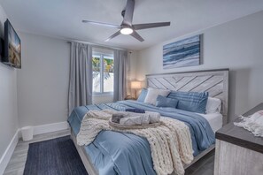 Ein modernes Schlafzimmer mit einem Bett, einem Deckenventilator, einem Fenster mit Vorhängen und einem Bild an der Wand.