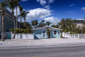 A small, light blue building with a white fence, surrounded by palm trees and a clear sky. - Retreat at Solace West-Hot Tub/Fire Pit/Sunsets (Holmes Beach)