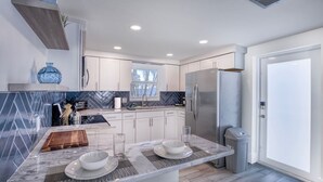 Una cocina moderna con armarios blancos, encimera de mármol y refrigerador de acero inoxidable.