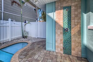 A swimming pool with a tiled border, a white picket fence, and a tiled wall with a circular design.