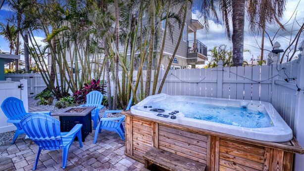 Un patio trasero con un jacuzzi, sillas azules y una terraza de madera.