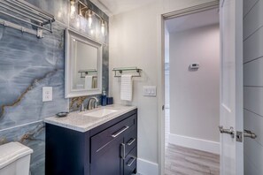 A modern bathroom with a marble backsplash, a large mirror, a sink with a faucet, and a shower area. - Retreat at Solace West-Hot Tub/Fire Pit/Sunsets (Holmes Beach)
