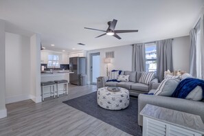 A modern living room with a grey sofa, a round ottoman, and a ceiling fan.